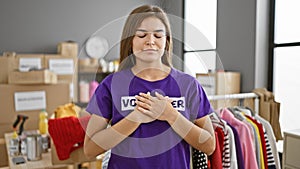 Emotional portrait of a beautiful, young hispanic woman working indoors at a charity center, hands on chest, closing her eyes in