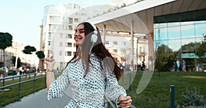 Emotional portrait of the cheerful attractive young brunette dancing while listening to music in headphones outdoor. 4k