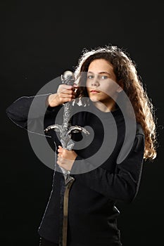 Emotional portrait of a girl with long curly hair with a sword on a black background