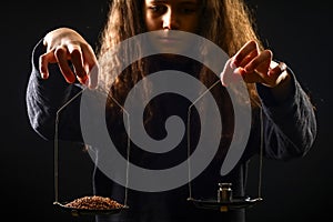 Emotional portrait of a girl with long curly hair weighing grain and weights on scales against a black background