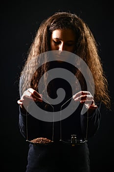 Emotional portrait of a girl with long curly hair weighing grain and weights on scales against a black background