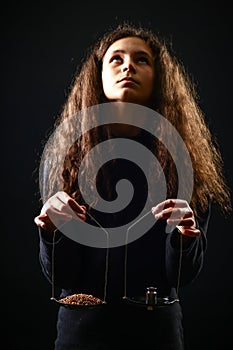 Emotional portrait of a girl with long curly hair weighing grain and weights on scales against a black background