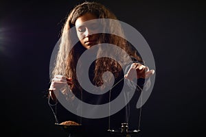 Emotional portrait of a girl with long curly hair weighing grain and weights on scales against a black background