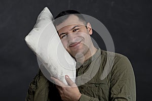 Emotional portrait of a happy man 30-35 years old, pressing a pillow to his face on a black background.