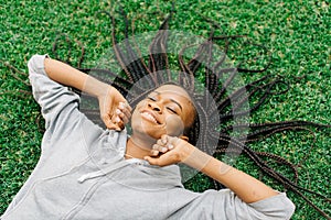 Emotional portrait of the joyful afro-american woman moving hands while laying on the grass and listening to music.