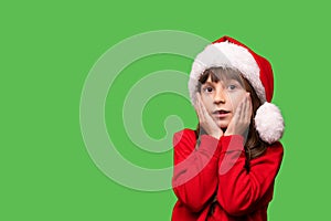 Emotional portrait. A little girl in a Santa hat holds her hands near her face in surprise. Christmas and New Year