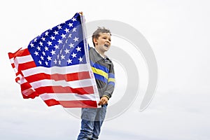 Emotional portrait of patriotic american boy holding USA flag waving in the wind. Patriotic holiday. USA celebrate 4th of July