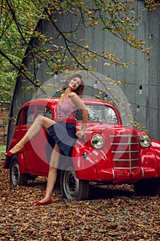 Emotional portrait. Pin-up girl posing near by a red russian retro car.The model laughs loudly, flirtatiously showing slender legs