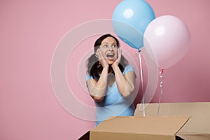 Emotional pregnant woman expressing happy surprise while pink and blue balloons appears from a box, expecting twins.