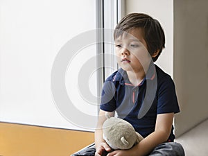 Emotional portrait sad kid sitting with teddy bear, Lonely kid sitting on floor in corner and looking down,Little boy wall corner
