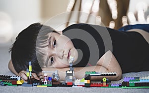 Emotional portrait Unhappy kid lying down on wooden floor with his plastic blocks toy, Candid shot lonely Child boy with sad face