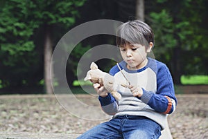 Emotional portrait of unhappy kid sitting with dog toy and playing wooden stick in playground, Lonely littel boy looking sad