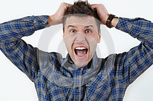 Emotional portrait of young angry screaming man pulling his hair