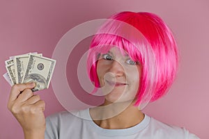 portrait of a young beautiful happy woman with pink hair holding dollars on a pink background