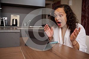 Emotional portrait of a young woman in white bathrobe, expressing amazement astonishment looking at the digital tablet