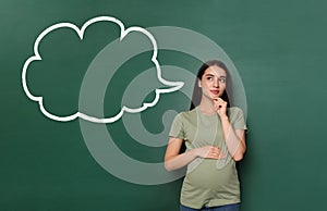 Emotional pregnant woman choosing name for her child. Future mother near green chalkboard with empty thought cloud