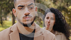 Emotional quarrel of hispanic couple outdoors angry girlfriend in background yelling and scolding boyfriend upset