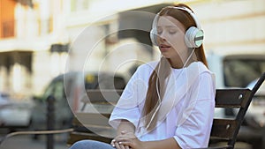 Emotional sad teenager girl in headset listening to lyric song outdoor music app