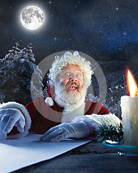 Emotional Santa Claus congratulating with New Year and Christmas, writing a letter, wish list in midnight with candle