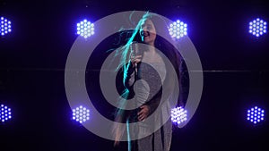 Emotional sexy singer sings song into vintage microphone in dark studio against background of blue lights. A woman in