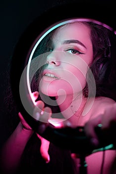 Emotional studio portrait of a young woman in a wireless headphones with ring flash effect. Round LED Circle Lamp.