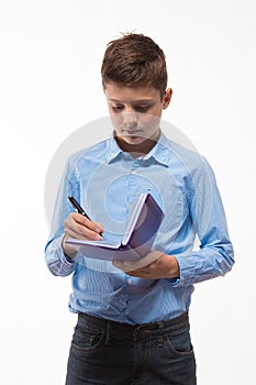 Emotional teenager boy brunette in a blue shirt with a diary and a pen in hand