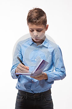 Emotional teenager boy brunette in a blue shirt with a diary and a pen in hand