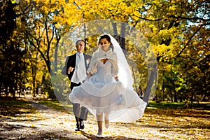 Emotional wedding portrait of the handsome groom running after the beautiful gorgeous bride along the autumn park.