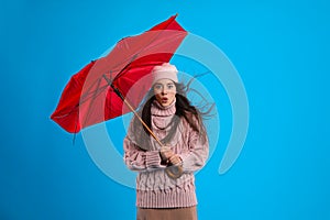 Emotional woman with broken umbrella caught in gust of wind on light blue background