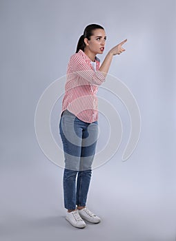 Emotional woman pointing with index finger on light grey