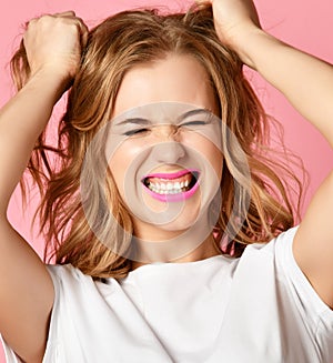 Emotional woman screaming shouting yelling closeup portrait on pink background pull tearing head hair.