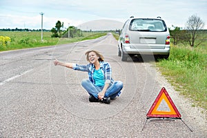 Emotional woman sitting on road near emergency sign thumbs up