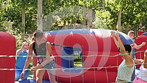 Emotional woman tied with rope to her friend competing to collect hoops on inflatable playground on sunny summer day