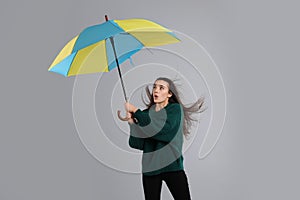 Emotional woman with umbrella caught in gust of wind on grey background