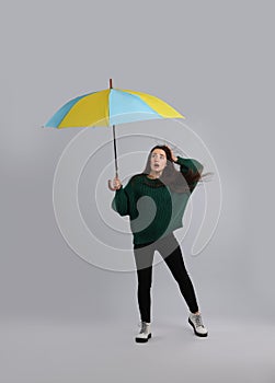 Emotional woman with umbrella caught in gust of wind on grey background