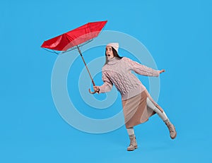 Emotional woman with umbrella caught in gust of wind on light blue background