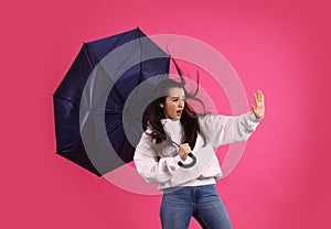 Emotional woman with umbrella caught in gust of wind on pink background