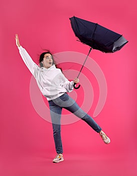 Emotional woman with umbrella caught in gust of wind on pink background