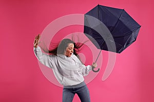 Emotional woman with umbrella caught in gust of wind on pink background