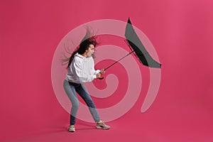 Emotional woman with umbrella caught in gust of wind on pink background