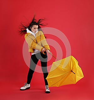 Emotional woman with umbrella caught in gust of wind on red background