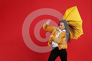 Emotional woman with umbrella caught in gust of wind on red background. Space for text