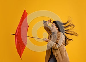 Emotional woman with umbrella caught in gust of wind on yellow background