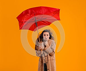 Emotional woman with umbrella caught in gust of wind on yellow background