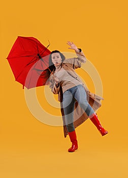 Emotional woman with umbrella caught in gust of wind on yellow background