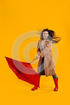 Emotional woman with umbrella caught in gust of wind on yellow background