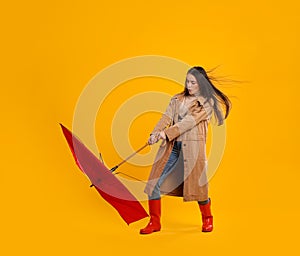 Emotional woman with umbrella caught in gust of wind on yellow background