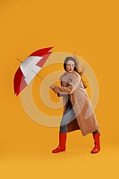 Emotional woman with umbrella caught in gust of wind on yellow background