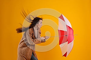 Emotional woman with umbrella caught in gust of wind on yellow background