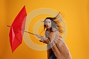 Emotional woman with umbrella caught in gust of wind on yellow background